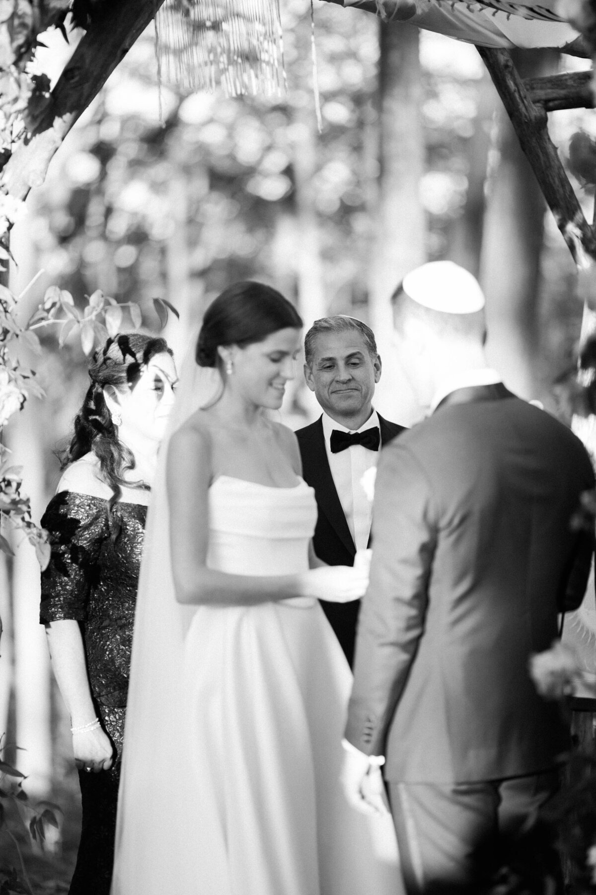 he bride smiling as she holds her groom’s hands under the chuppah