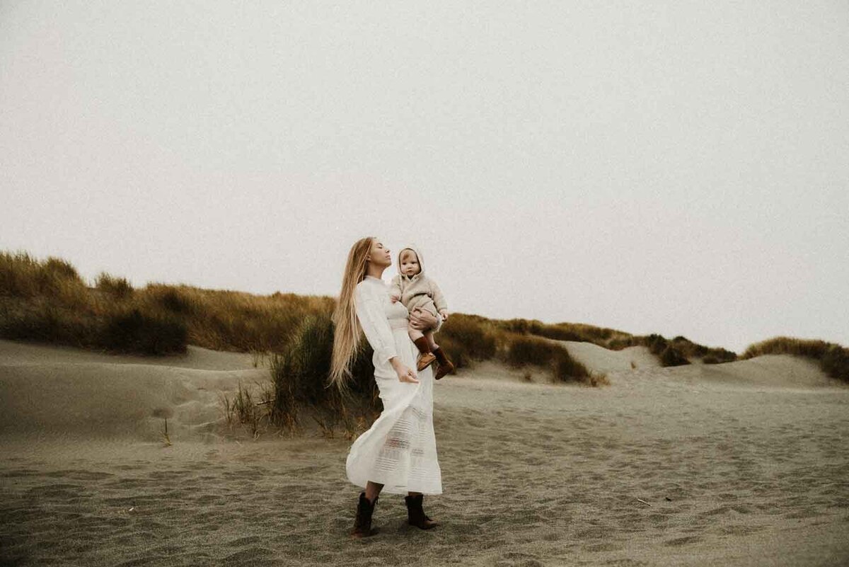 Oregon-Coast-workshop-mom-in-white-dress-holding-baby-in-dunes-Missouri-candid-fine-art-photographer