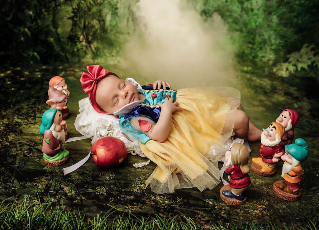 Newborn girl posed on a bed dressed as Snow White surrounded by the 7 dwarfs at her Toronto Newborn Photographer photo session.