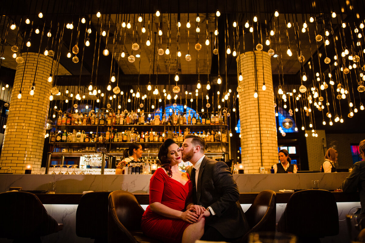 Engagement photo at the Foundation Hotel in Detroit Michigan. The couple sits at the bar in a red dress.  Photo By Adore Wedding Photography. Toledo Wedding Photographers