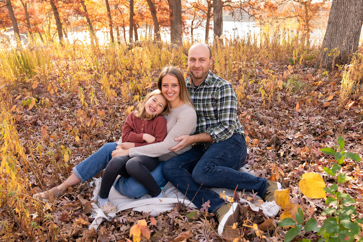 Family of three cuddles together on a blanket for their family photos at Silverwood Park in Minneapolis, Minnesota