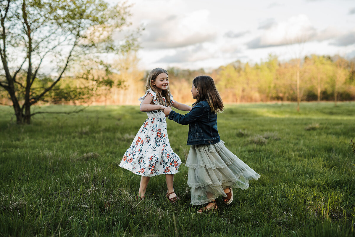 Two little girls twirling in a field in the spring time.