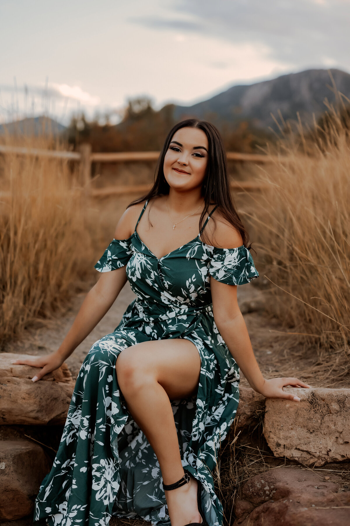 High school senior girl sitting on natural rock steps in a green and white long floral green dress