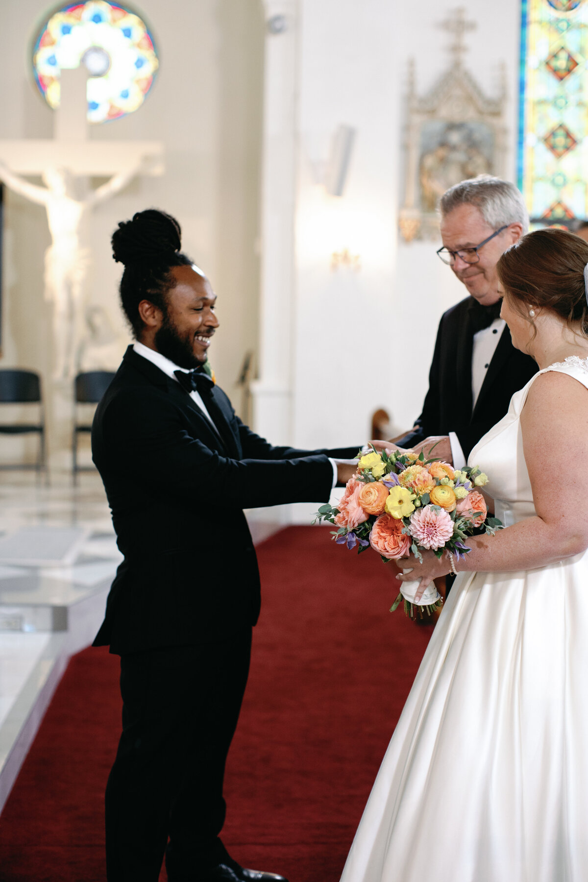 Groom in black tuxedo and bride in satin gown exchanging vows at Catholic church wedding in Washington DC.