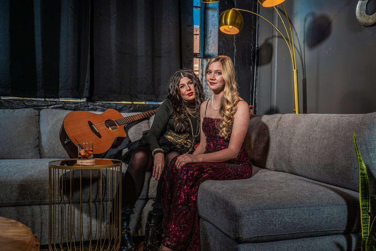 Two people sitting on a couch together with a guitar next to them 
