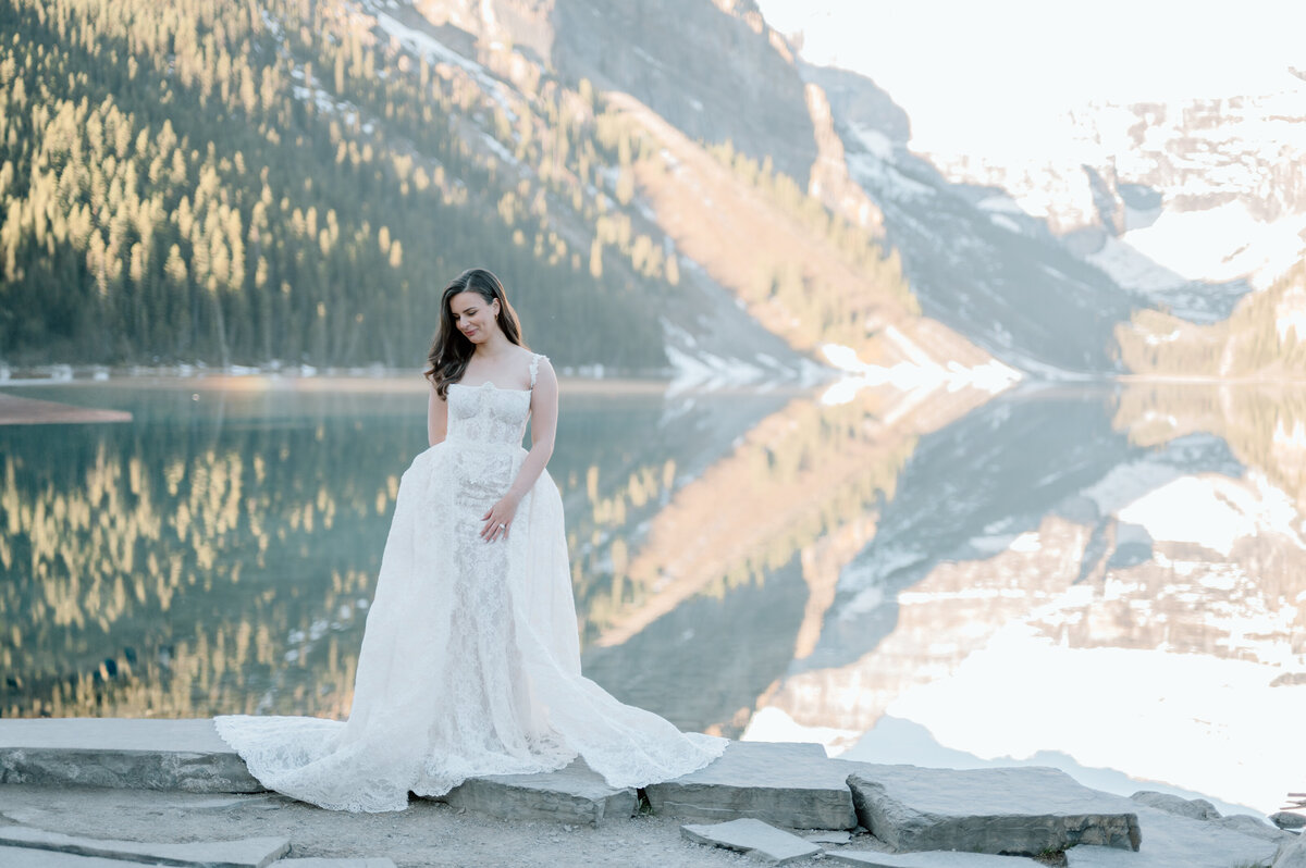 Bride standing on dock with clear lake reflection of mountains