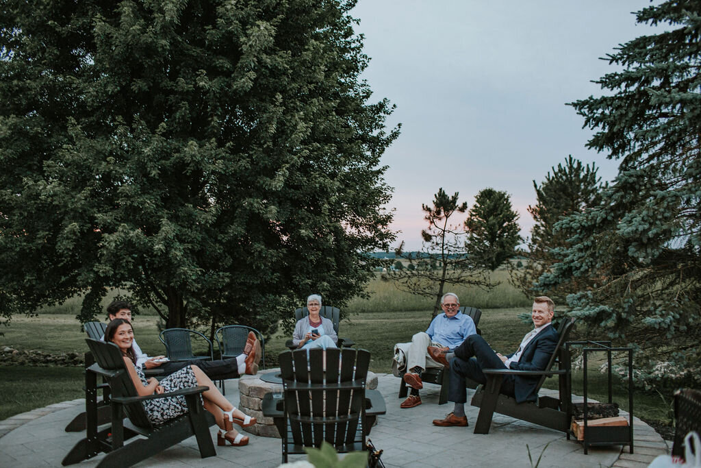 guests sitting in black  adirondack chairs around a smokeless stone firepit on the stone patio at Willowbrook wedding venue