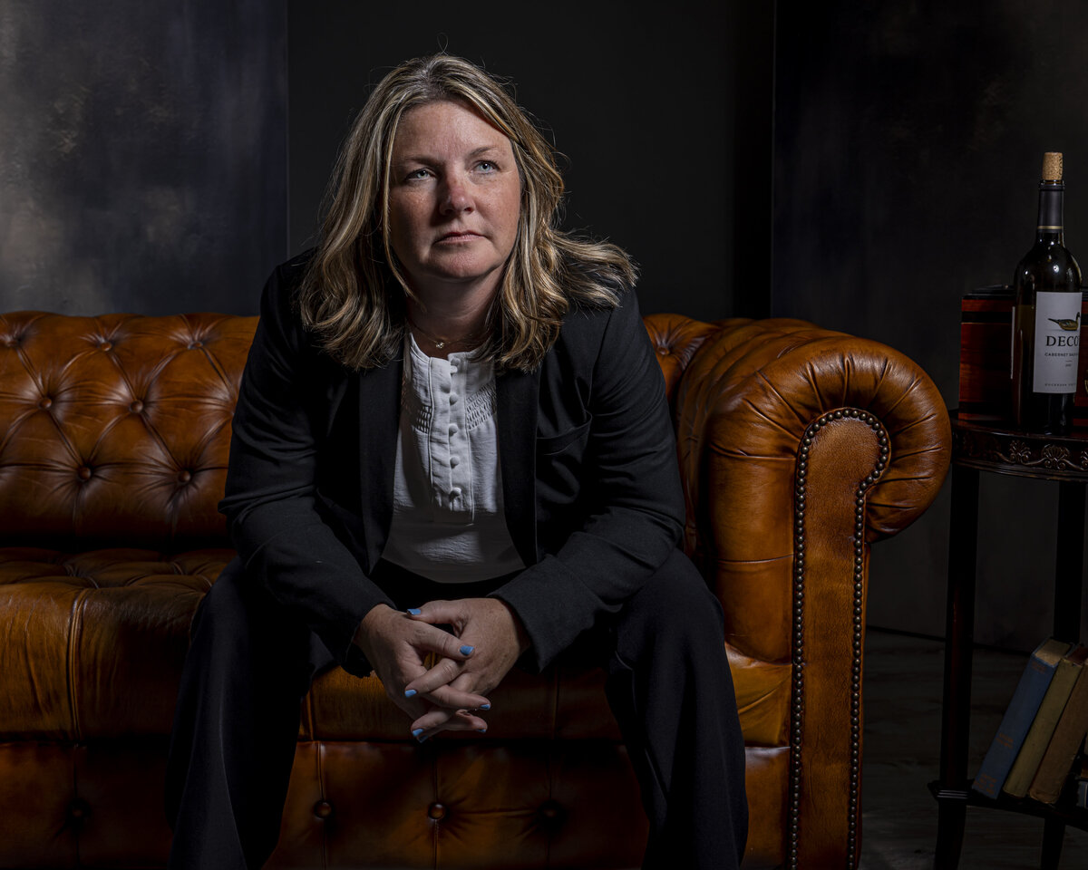 Headshot in MA of woman in black blazer seated on leather sofa, with warm lighting and dark backdrop by Rob Faber Photography.