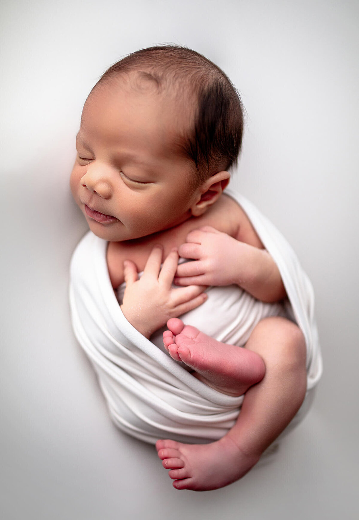 Soft natural detailed portrait of baby wrapped in white and showing hands, feet and face in studio newborn session located in Riverview, FL 