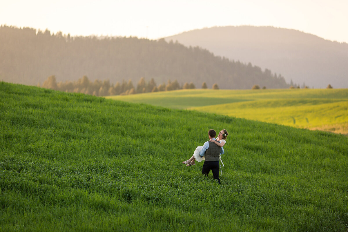 A groom carries his bride through a field following their wedding ceremony at Camp Four Echoes near Worley, Idaho.