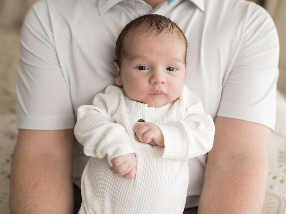 dad holding newborn baby boy in white onesie for studio photoshoot 