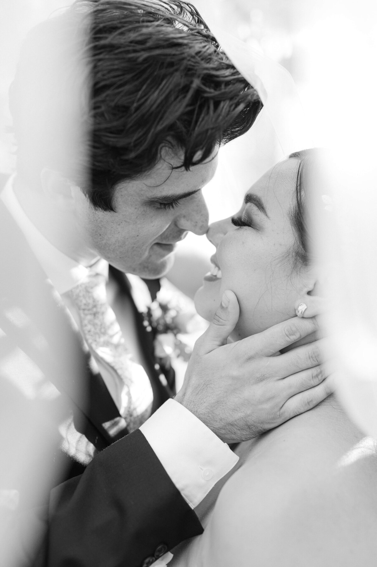 B&W image of a couple passionately kissing underneath a wedding veil.