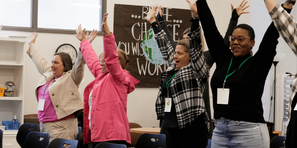 Photo of four women attendees at an Activate the Awesome keynote at the Fresh Take Conference. They're all smiling with both arms raised in celebration.