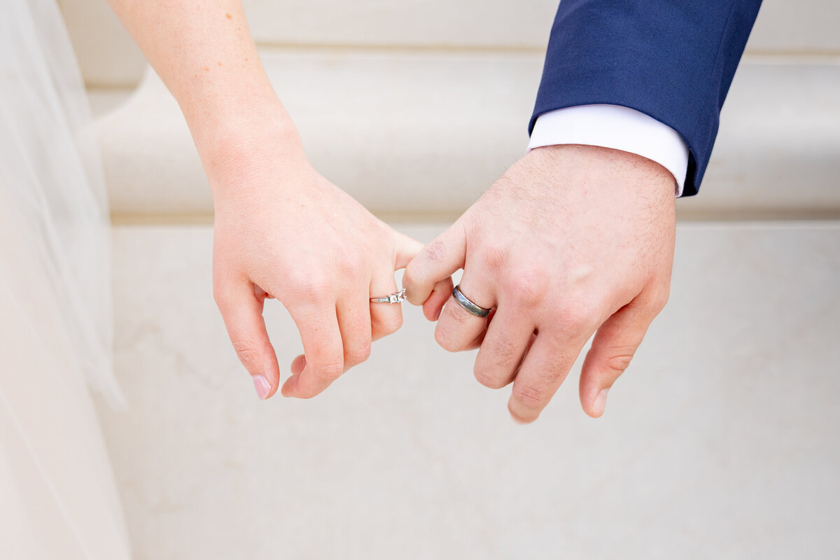Close-up of bride and groom linking pinkies to display their wedding rings on their special day.