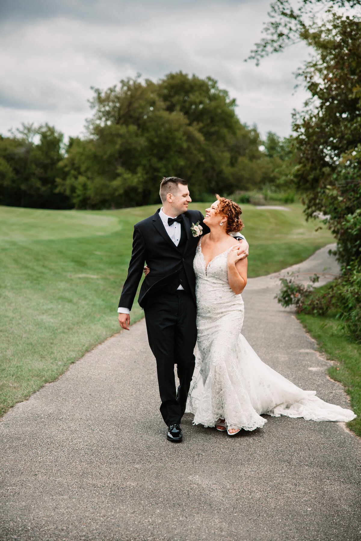 Newlyweds snuggle while walking and smiling at each other on a sidewalk