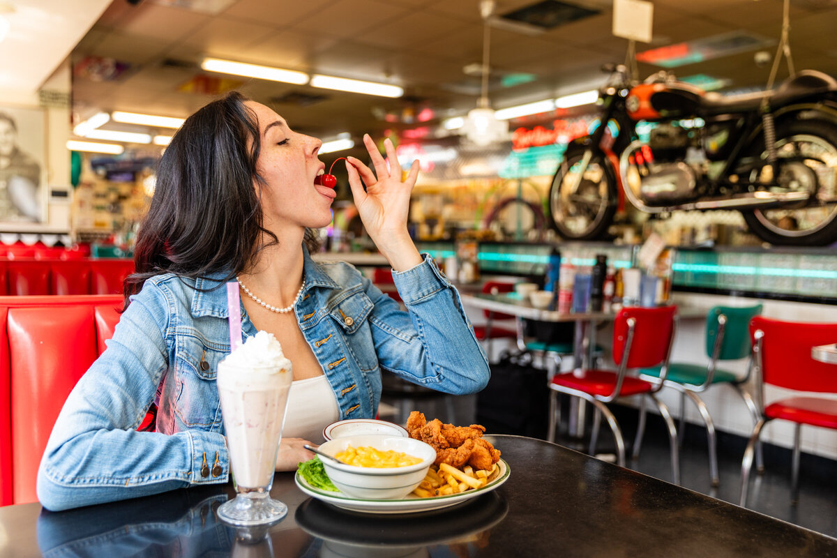 Photo of a woman eating the cherry off of her strawberry milkshake at a 50s diner in Littleton Colorado. 