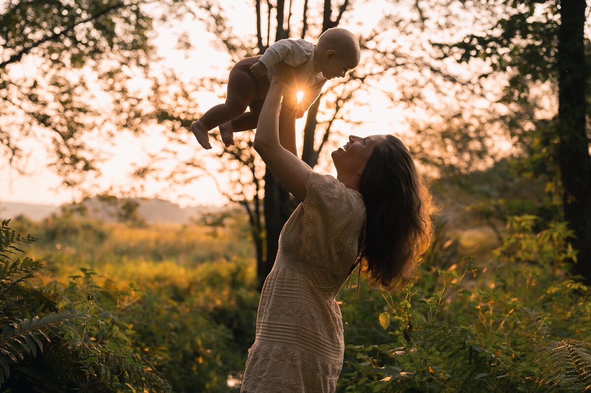 Mom holding baby with golden sun behind laughing having a happy family photo session