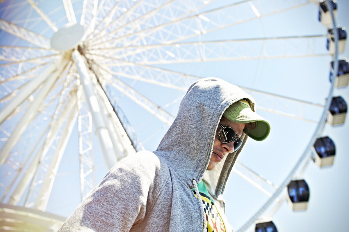 A person with their hood up with a ferris wheel behind them