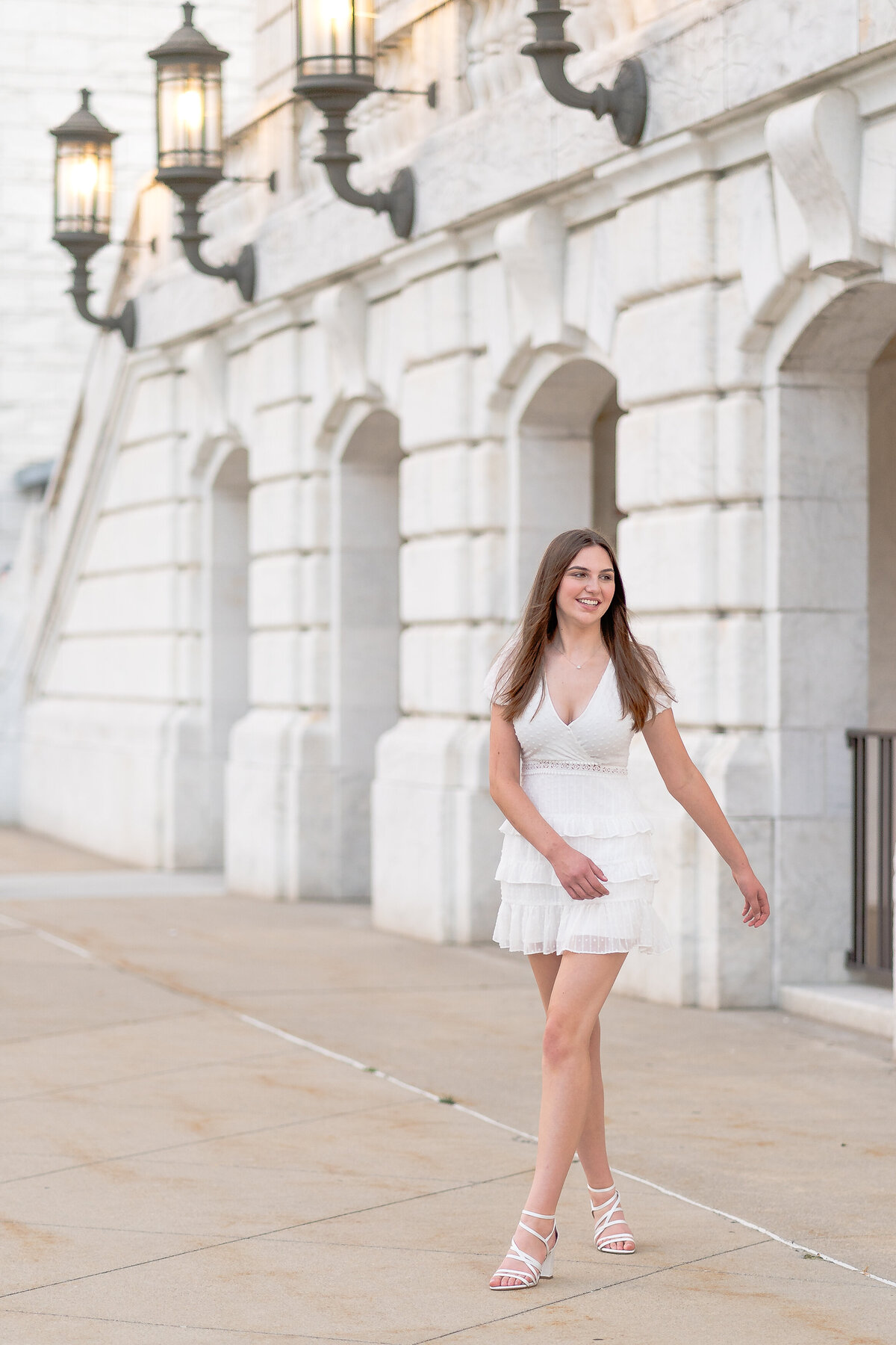 teenage girl in a white dress walking away from the Detroit Institute of Arts building as she sways her arms side to side 