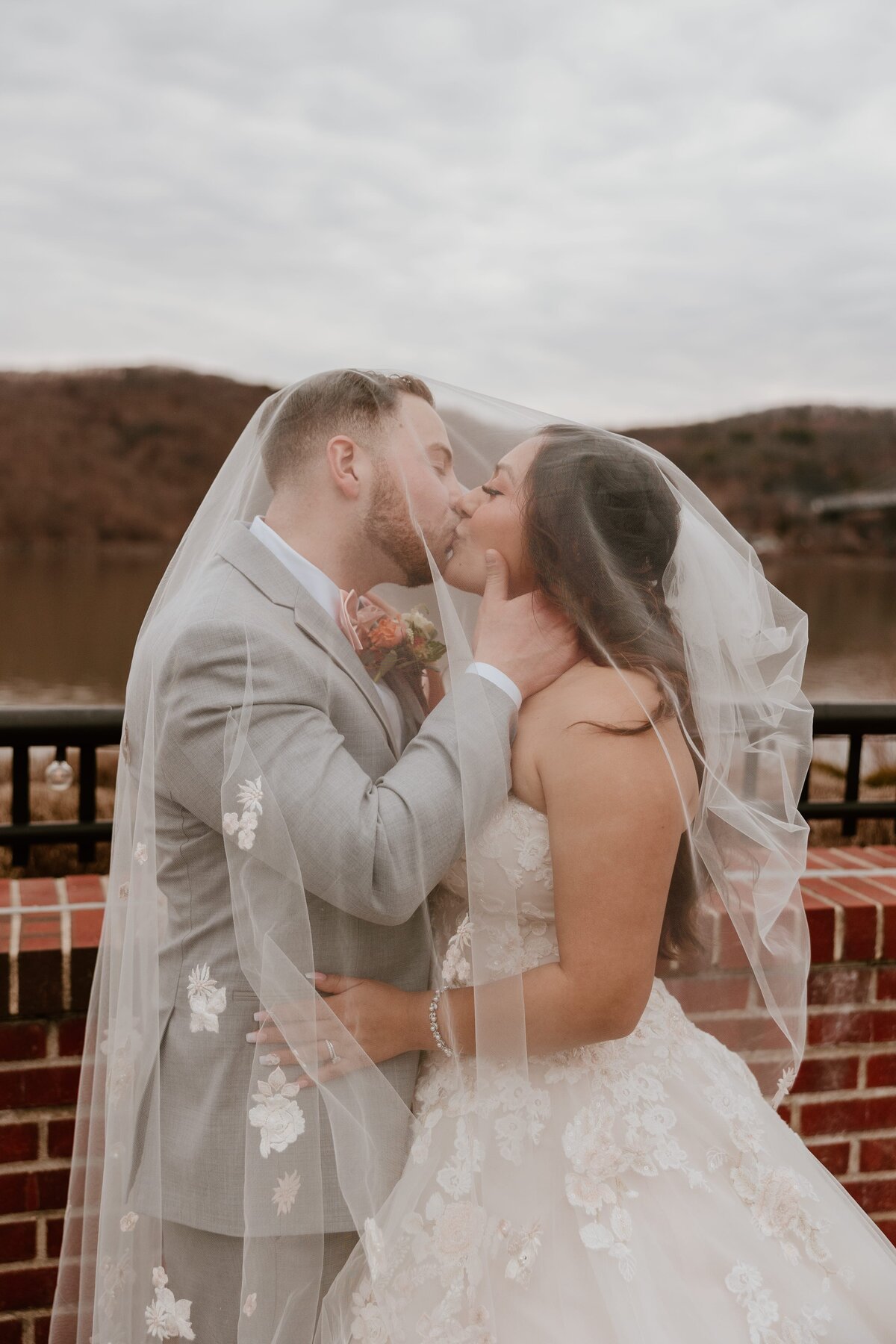 Bride and groom sharing a romantic kiss under the bride’s floral-embroidered veil at The Grandview in Poughkeepsie. Captured against a natural outdoor backdrop during a Hudson Valley wedding.
