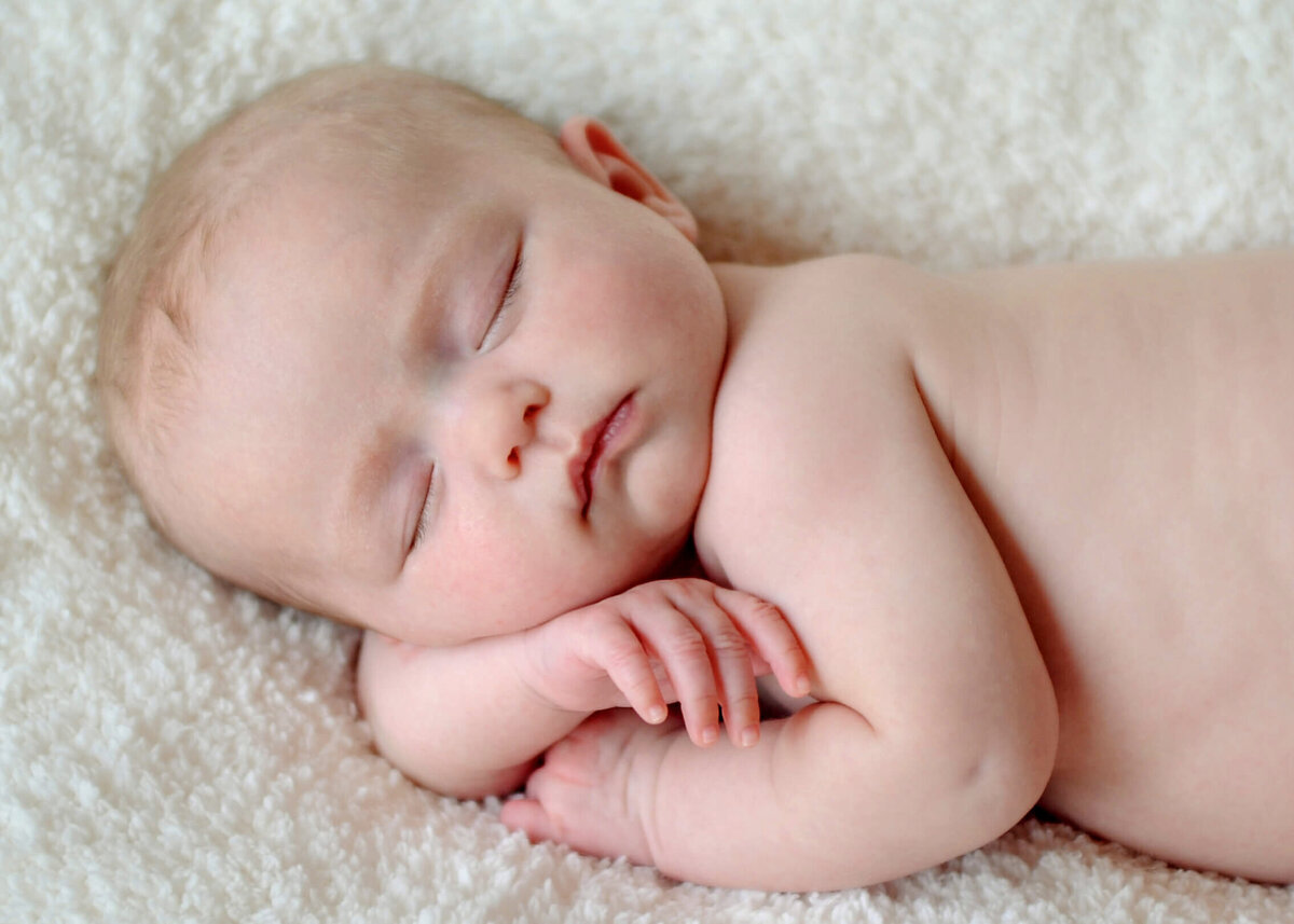 A close up of an adorable baby girl laying on her side on a white blanket.