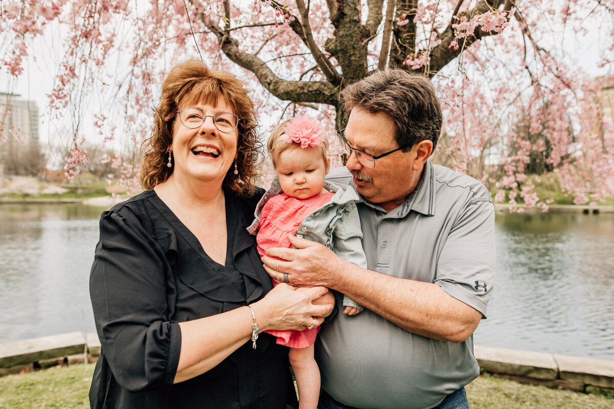 Grandmother and grandfather hold granddaughter outside.