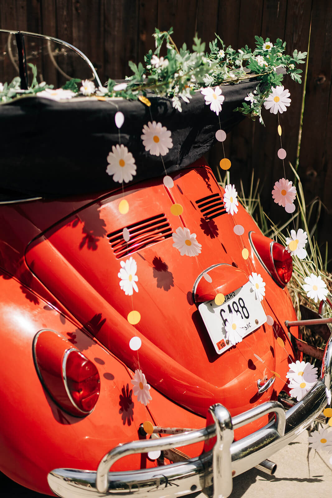 The back of a red car that is decorated with paper flower garlands.