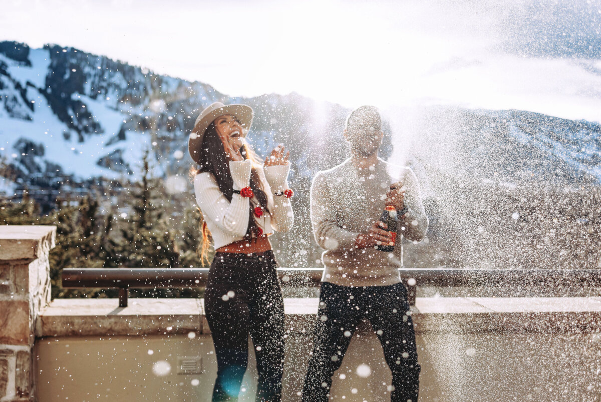 A couple sprays champagne into the air laughing and enjoying the moment after their engagement