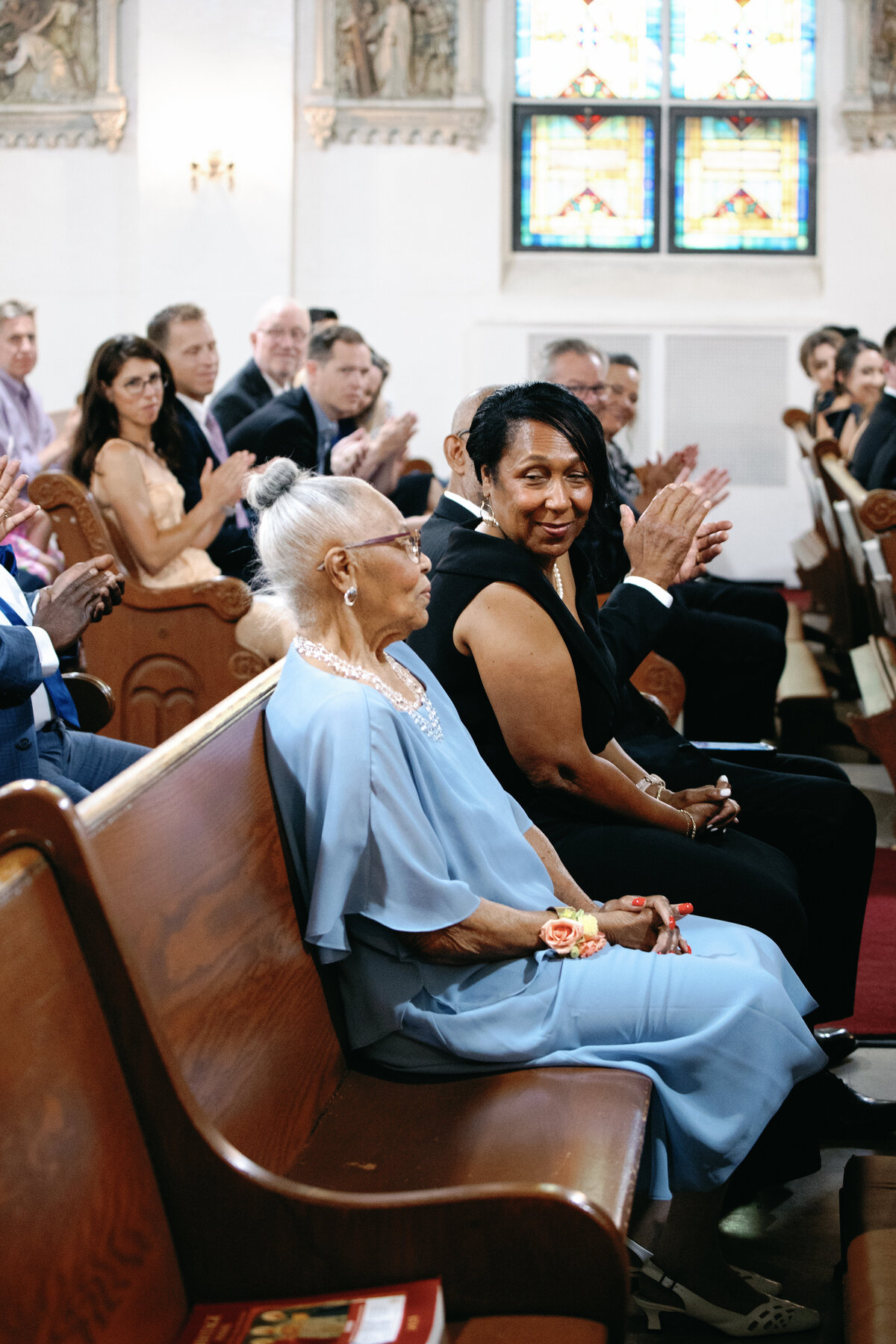 Family and friends seated in wooden pews smiling during Catholic wedding ceremony in Washington DC.