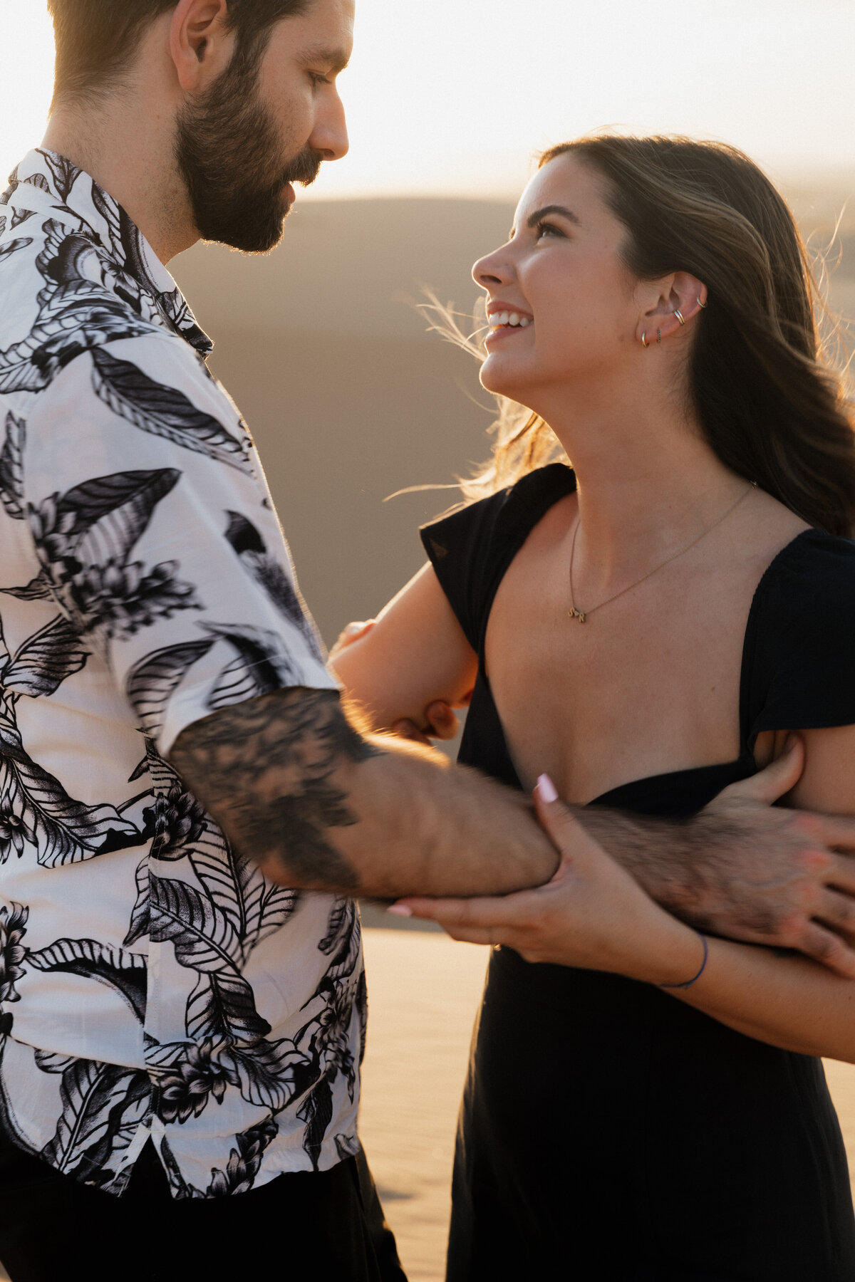 A candid moment of a couple smiling in the desert, bathed in golden light, captured with a refined fine art and documentary wedding approach.