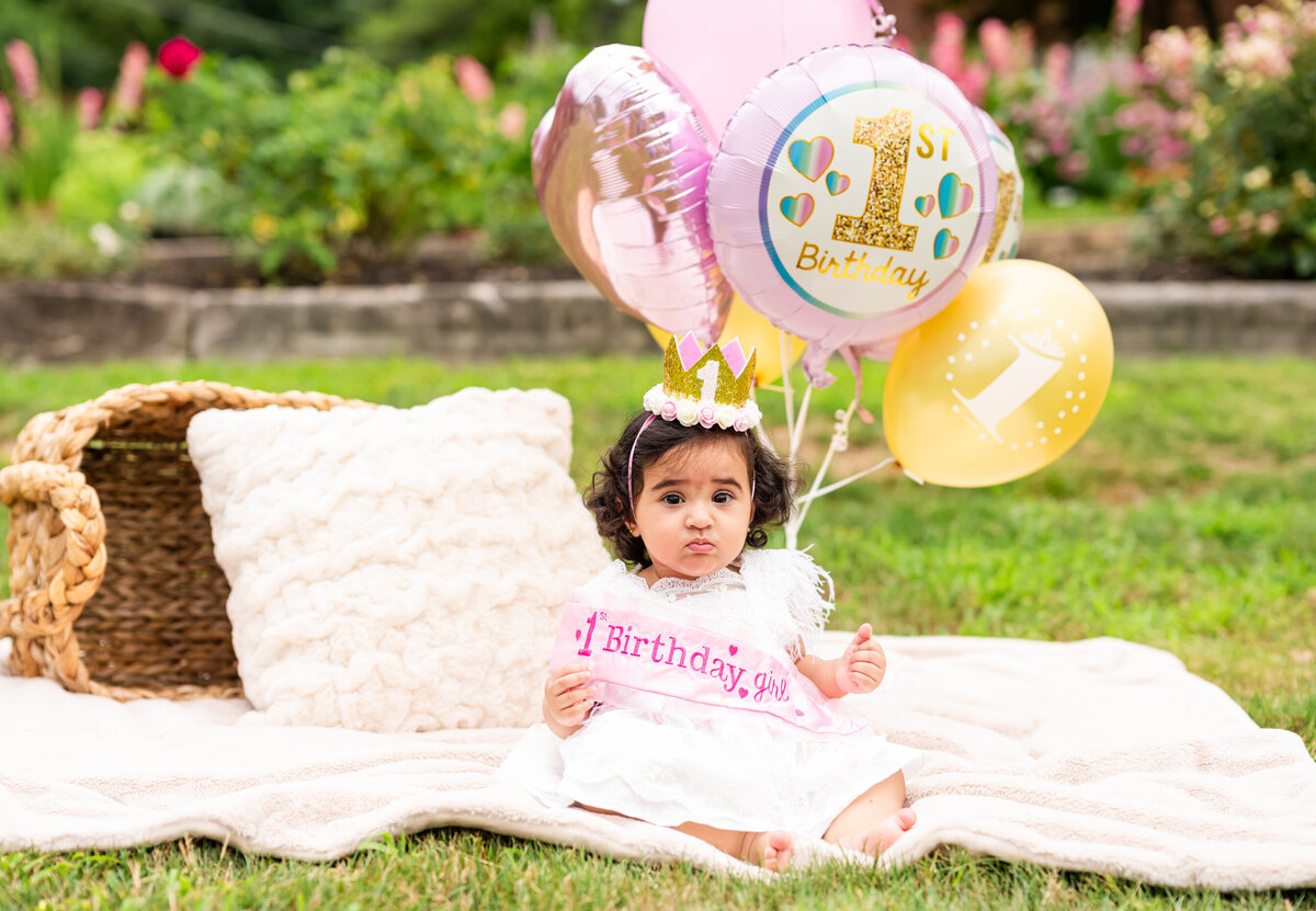 one year old girl with balloons sitting on blanket