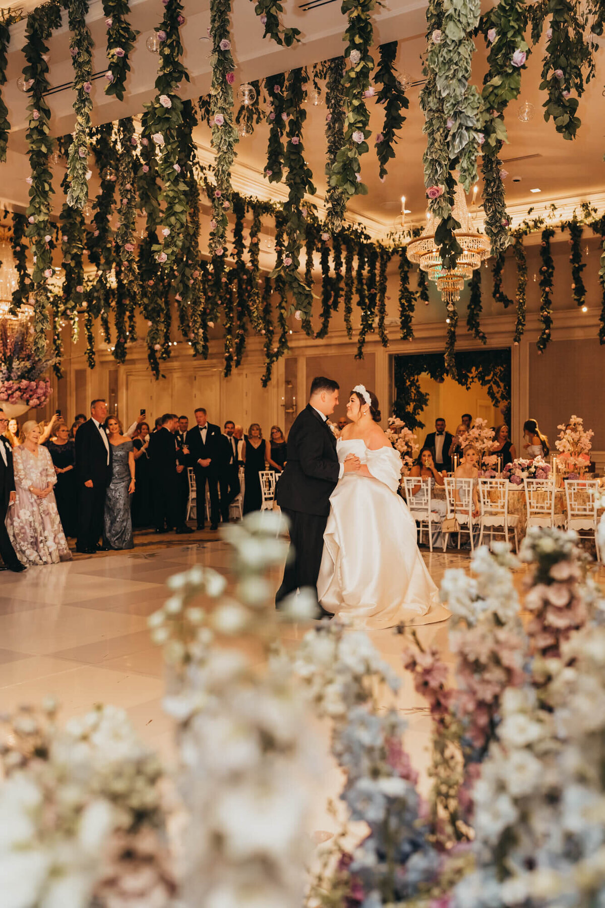 bride and groom share a first dance under hanging florals from the ceiling.