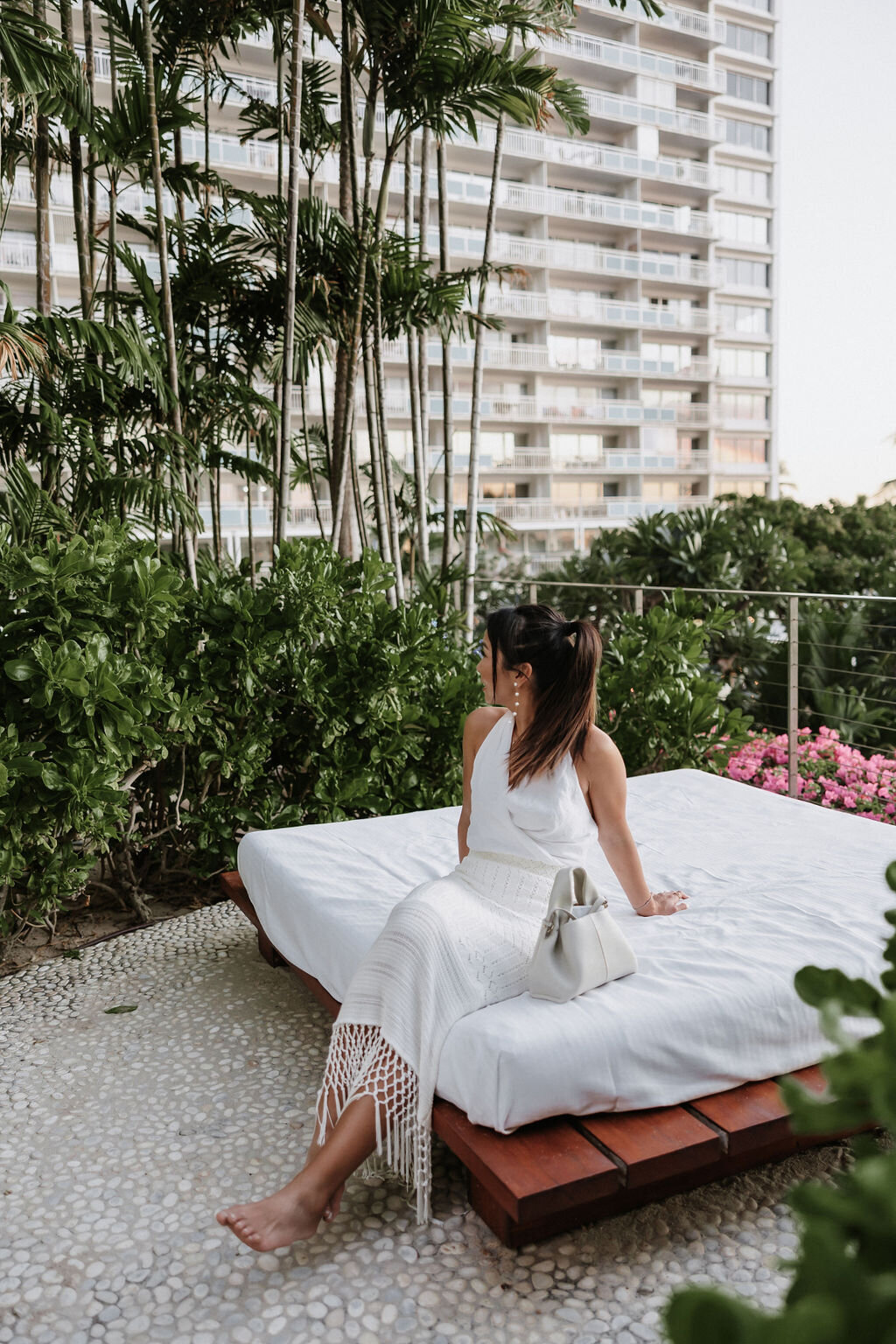 bride looking behind her reclining on white daybed with white tassel skirt, wrap top and small bag
