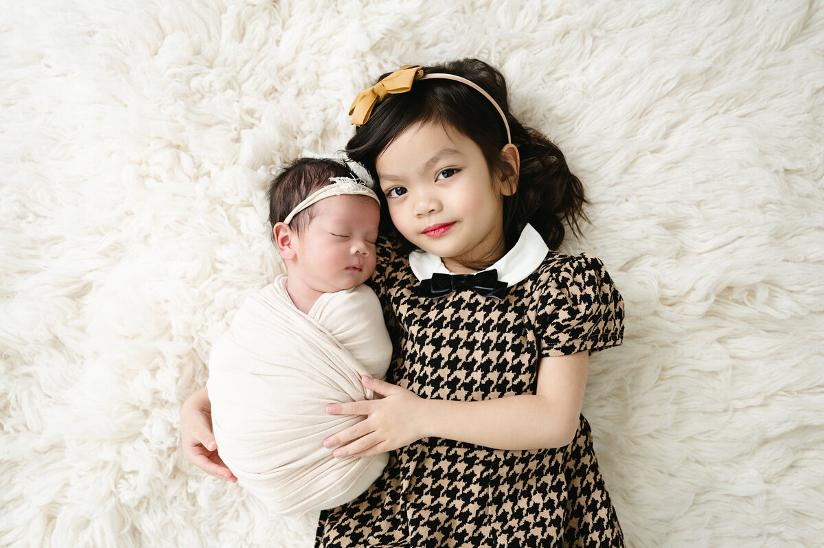 A heartwarming sibling moment captured in our Pittsburgh newborn photography session. The loving bond between siblings is beautifully preserved, with big sister holding her newborn baby sister.