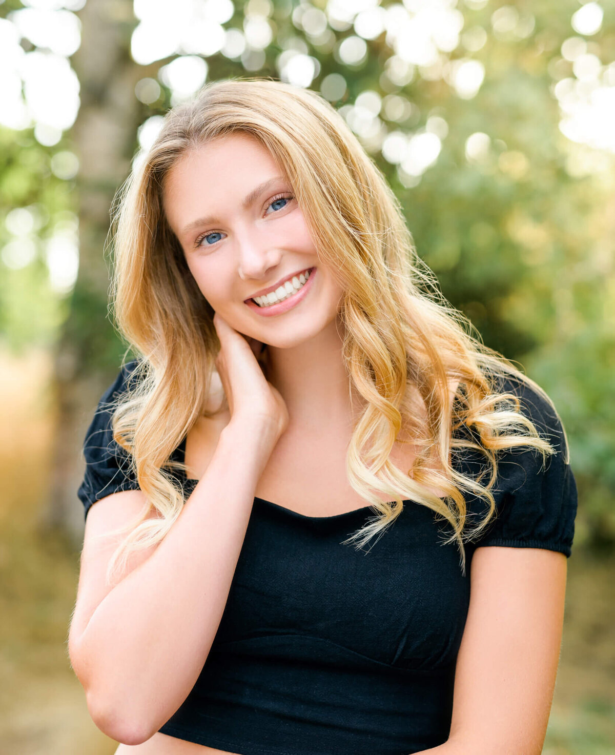 A teenage girl brushes her hair back while standing in a park at sunset