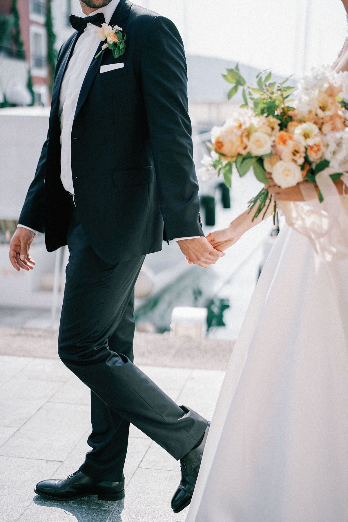 bride-groom-with-bouquet-walk-holding-hands-along-sea-cropped-faceless