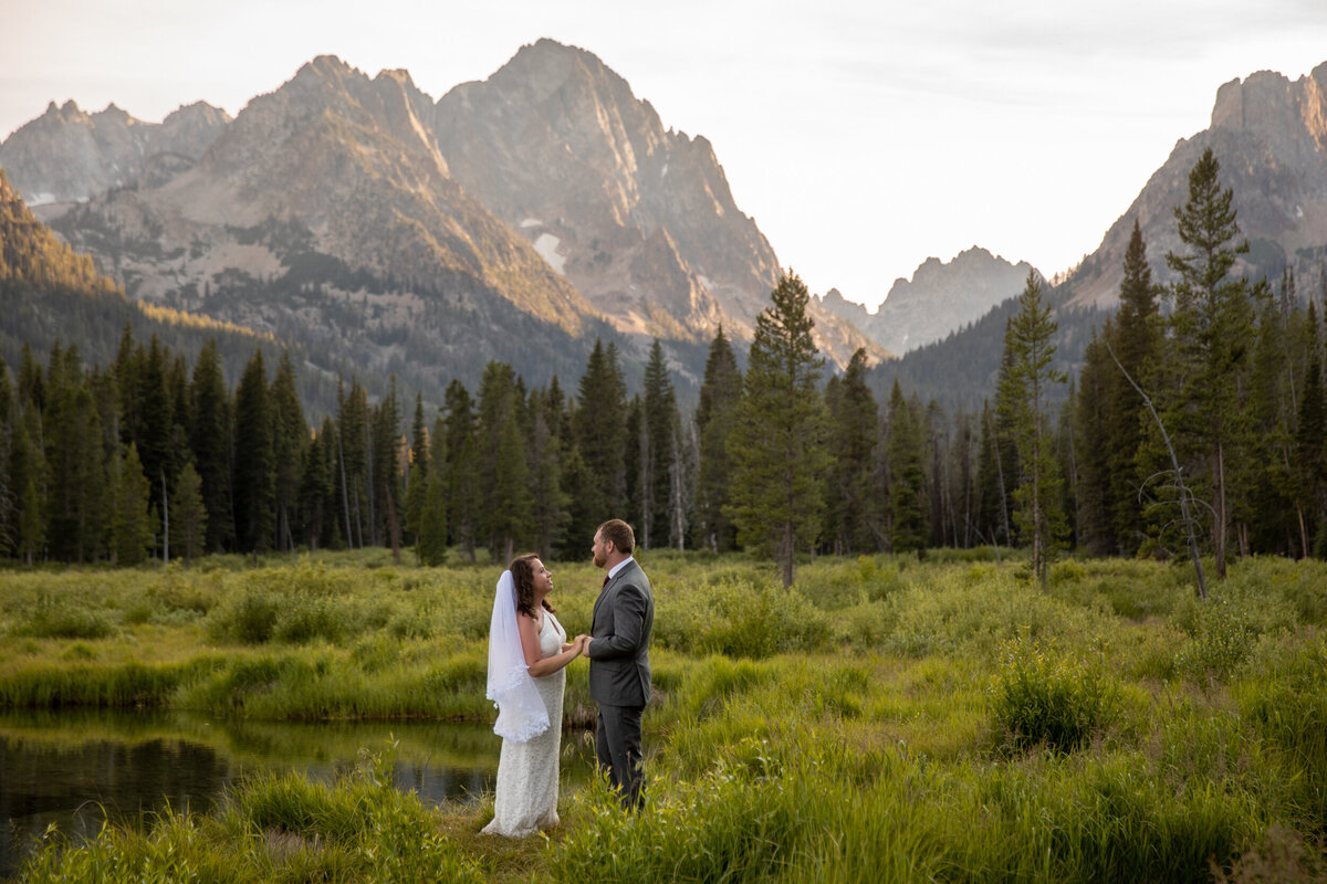 a bride and groom stand facing each other and holding hands next to a creek in Idaho.