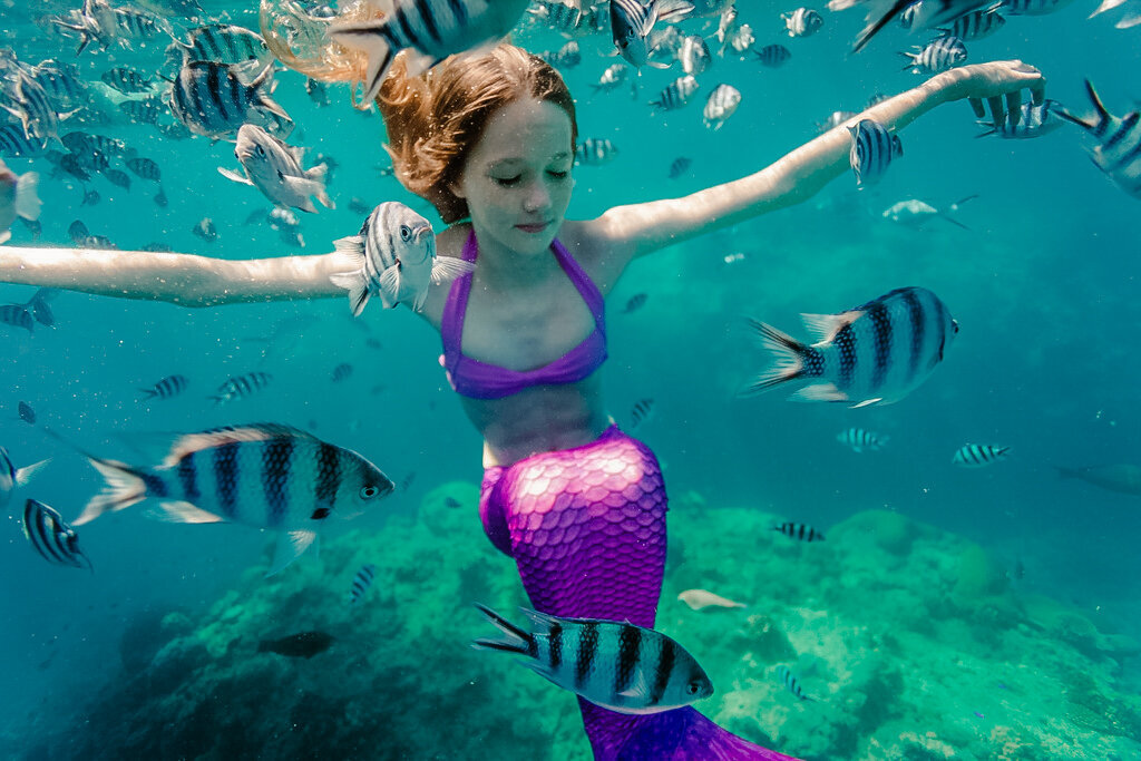 young girl in mermaid tail underwater with striped fish