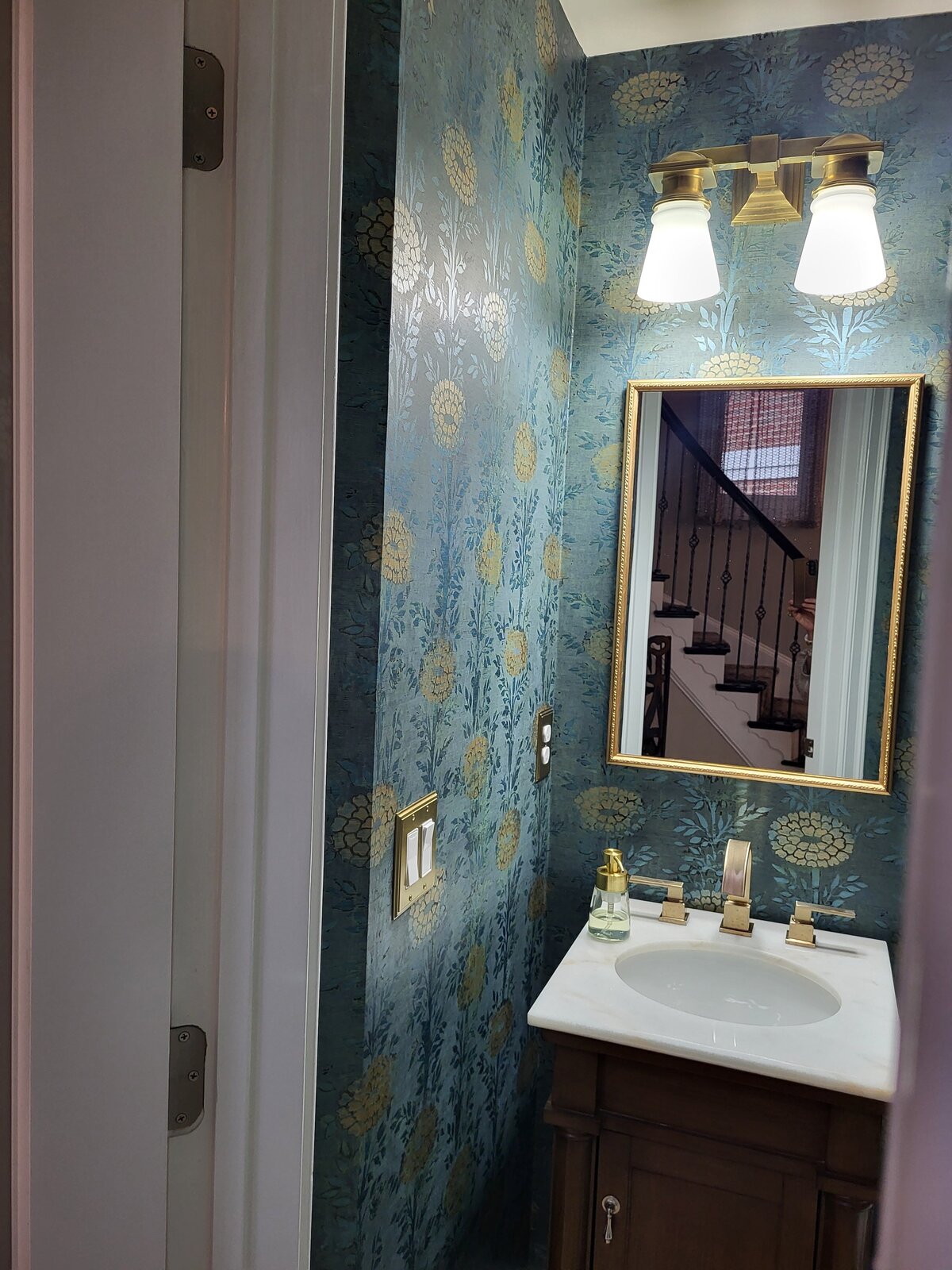 Wallpapered teal and gold chrysanthemum bathroom with brass lighting, mirror and sink fittings
