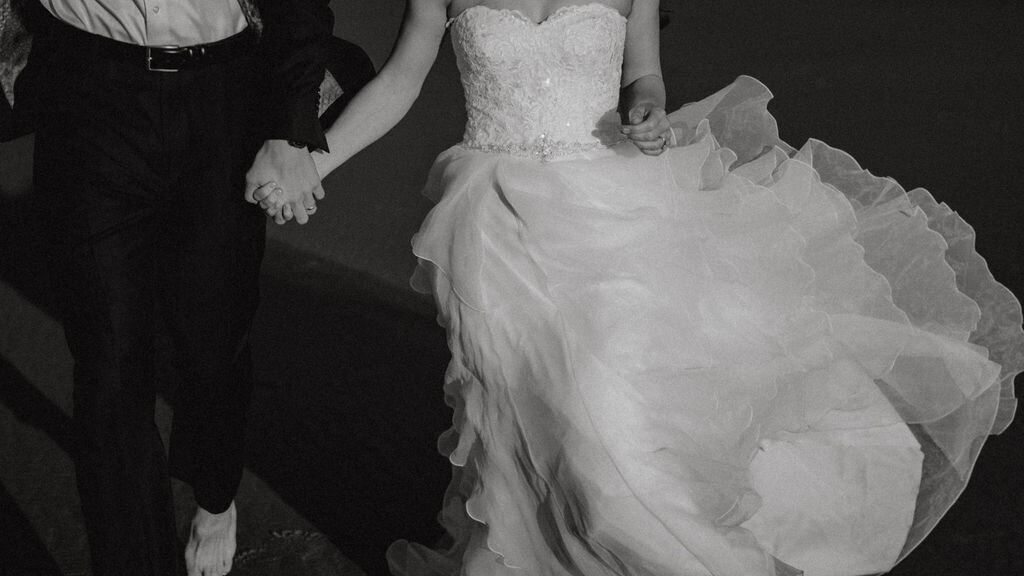 a close up of a bride and groom running on the beach in a dress and tuxedo