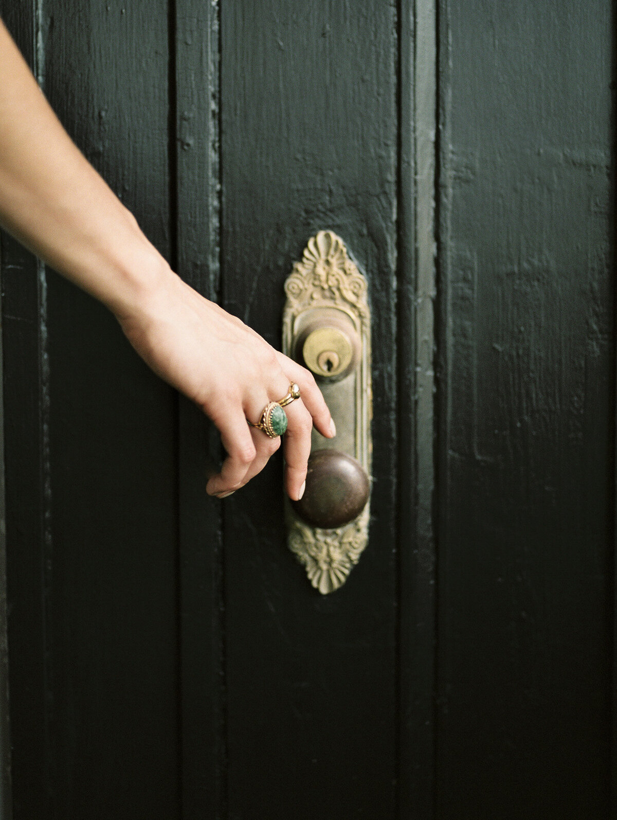 woman's hand with ornate gold rings, green stone, reaches for ornate historic doorknob in Detroit