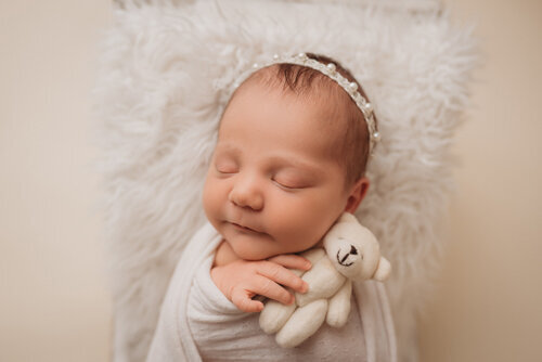 Baby girl sleeping for newborn portrait session with Atlanta Georgia newborn photographer snuggled up on her back on neutral fabric backdrop holding little white teddy bear