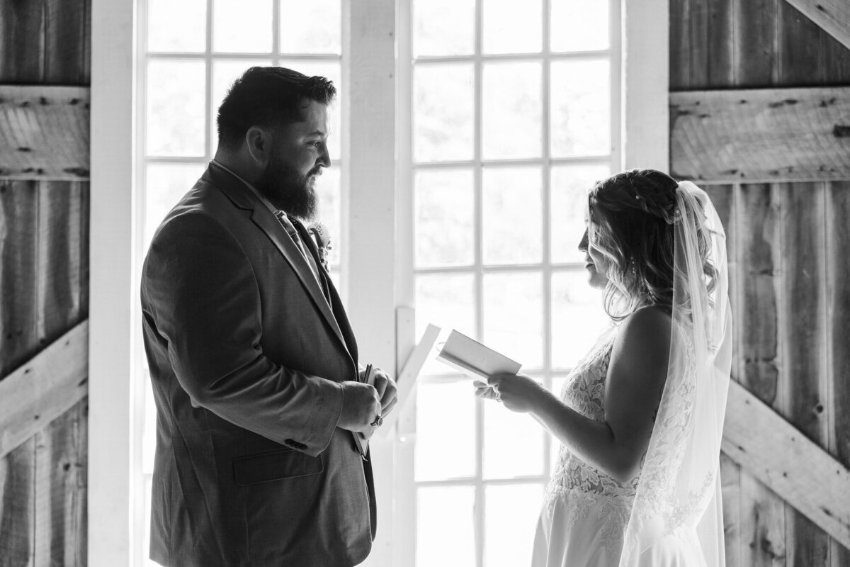 Black and white photo of a couple reading their vows in front of a bright window