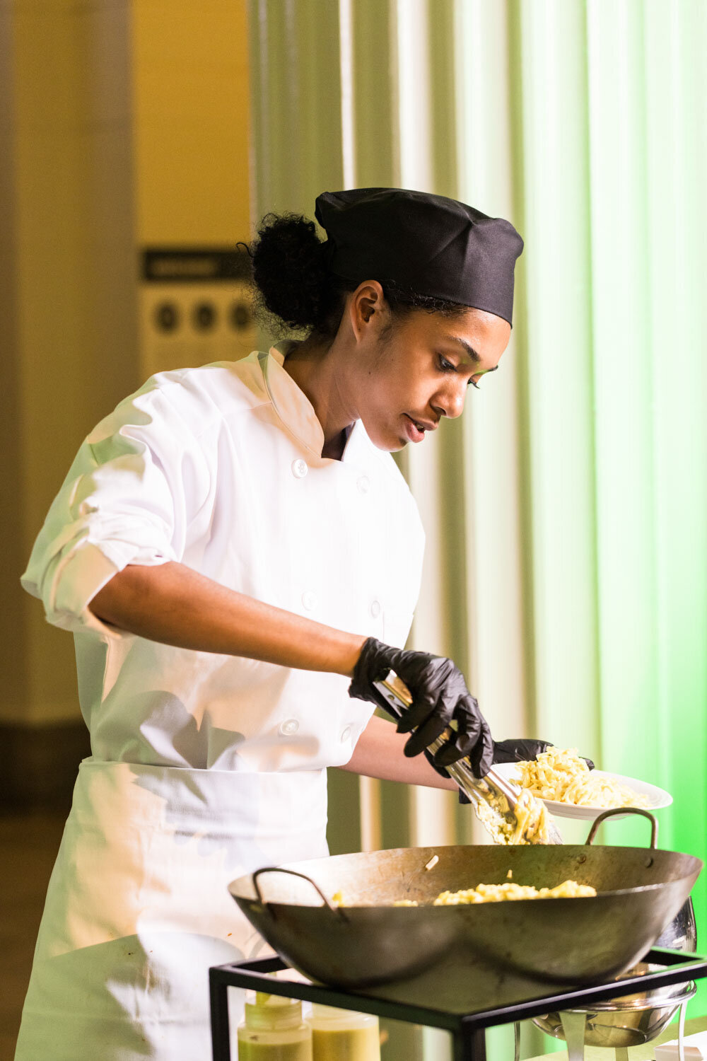 Female chef in uniform plating pasta with tongs