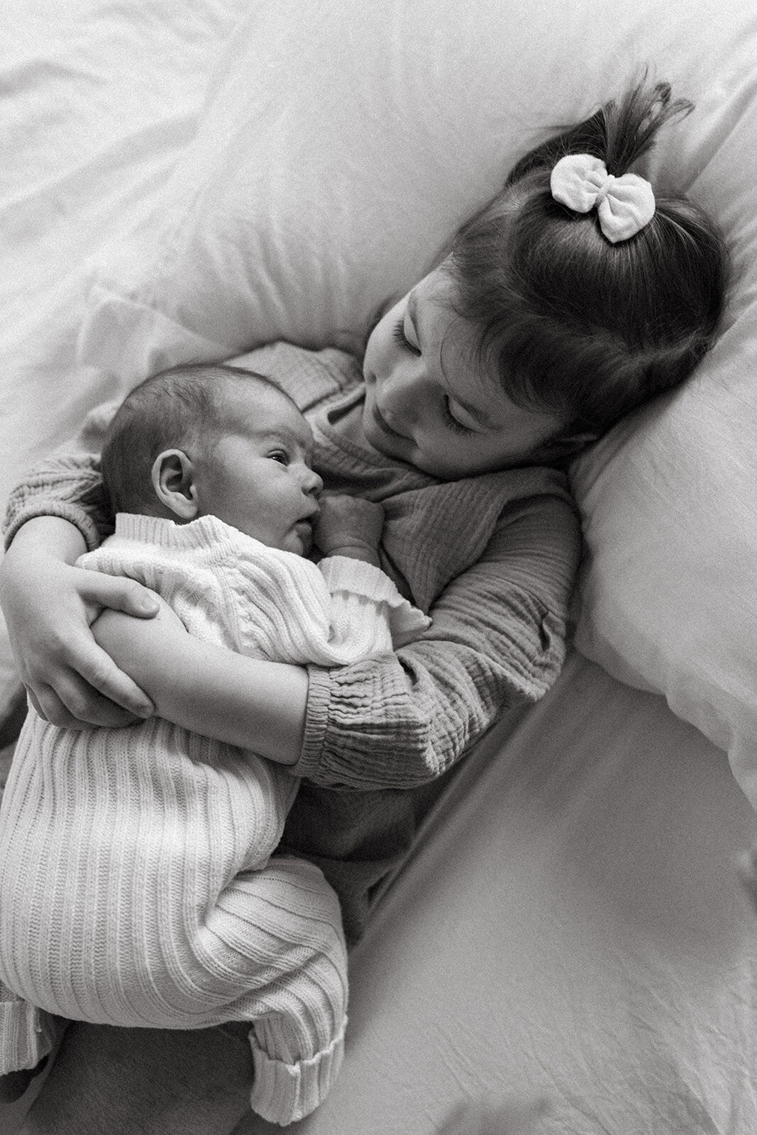 Young girl looking down affectionately at her baby brother laying on her chest during a relaxed family session