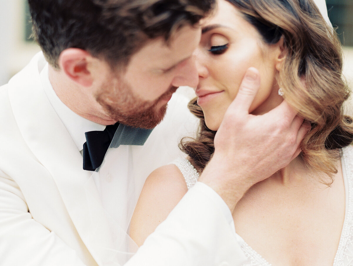 a groom in a white suit about to kiss his bride