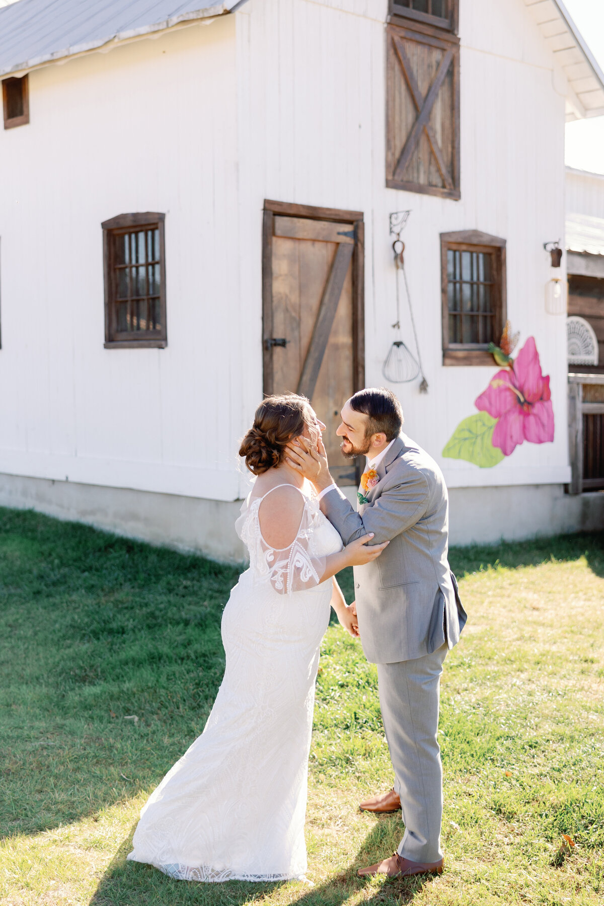 Bride and groom embracing in front of rustic white barn doors at The Hummingbird Chateau wedding venue.