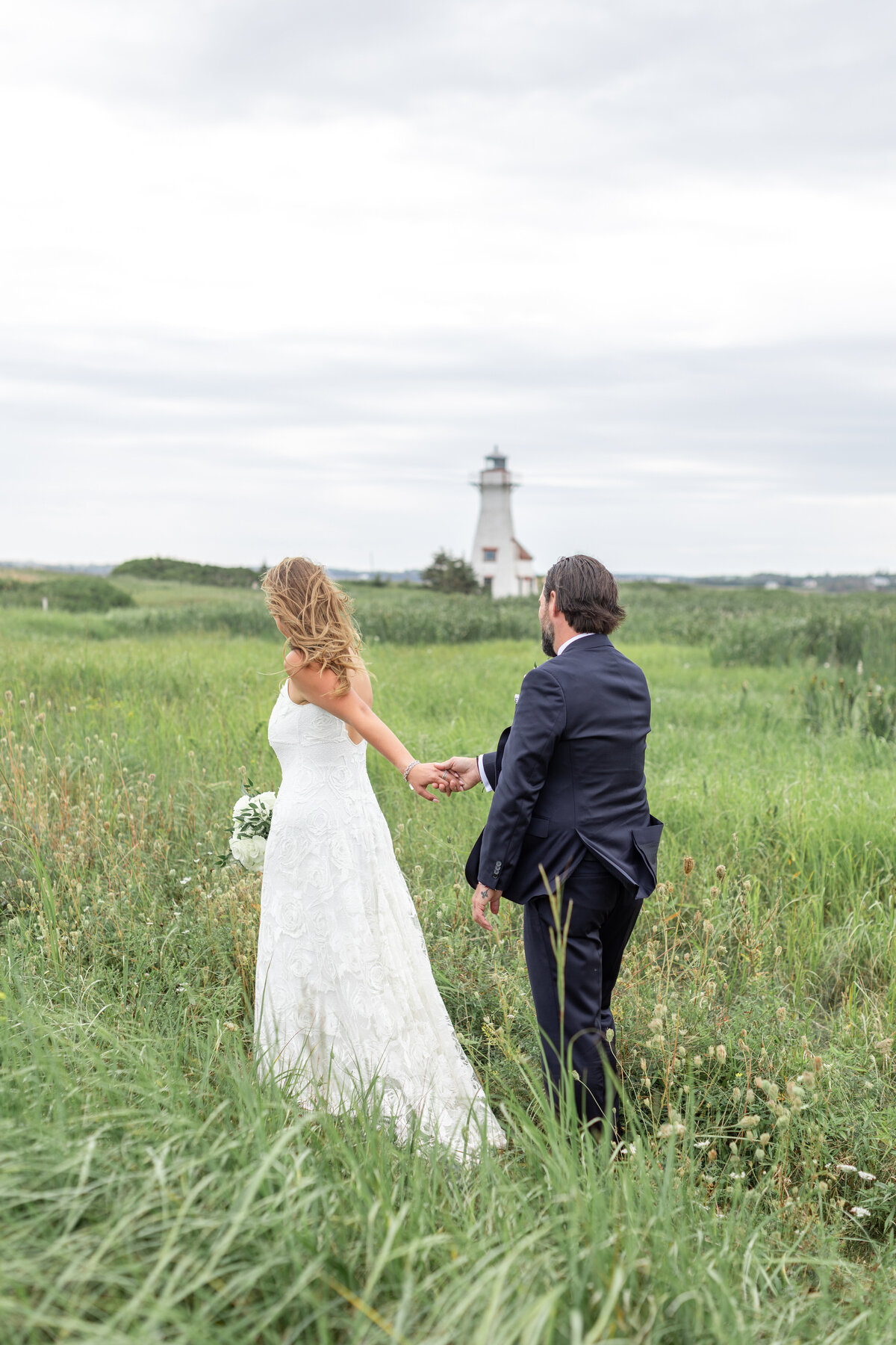 bride and groom walking in dunes overlooking PEI lighthouse