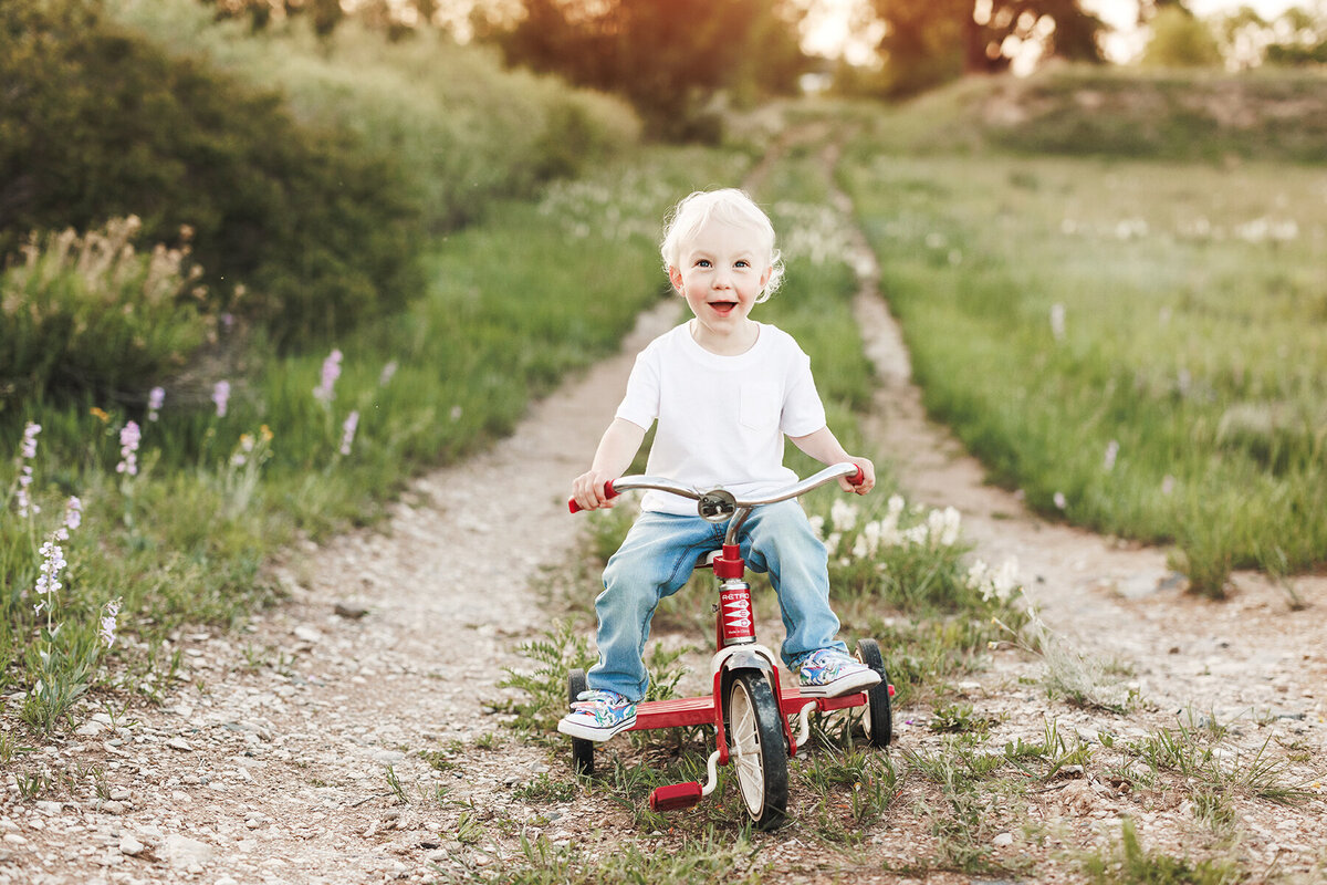 Little boy on a dirt road riding a red trike