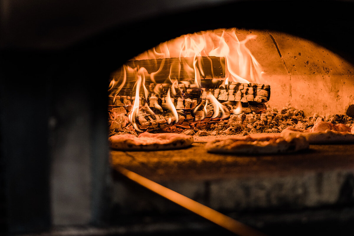 A close-up shot of a wood-fired pizza oven with flames rising around freshly baked pizzas, showcasing the rustic cooking style.